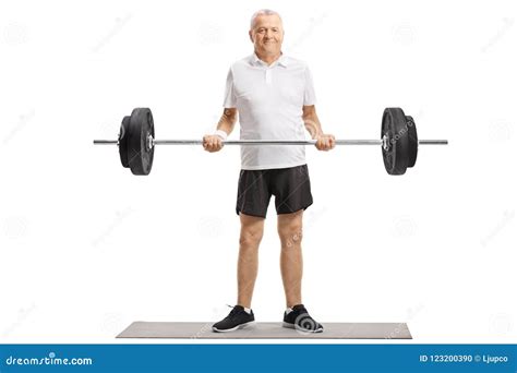 Senior Standing On An Exercise Mat And Lifting A Barbell Stock Photo