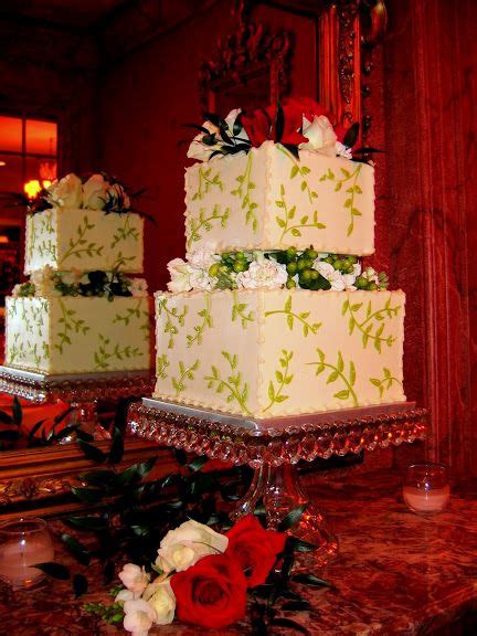 A Square Cake With Leafy Piping And Floral Spacers In Between