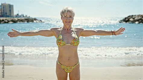 Middle Age Blonde Woman Tourist Wearing Bikini Smiling Confident With Arms Open At The Beach
