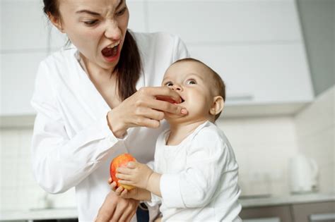 Jeune Belle Mère Nourrir Avec Pêche Son Petit Fils Dans La Cuisine