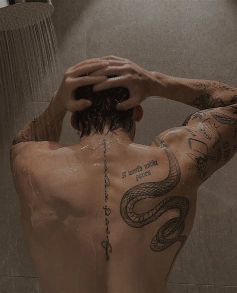 A Man With Tattoos On His Back Standing In Front Of A Shower Head And Arm