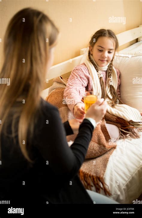 Portrait Of Caring Mother Giving Hot Tea To Sick Daughter Resting In