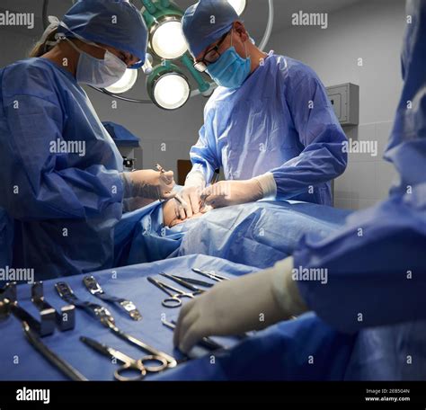 Medical team in surgical suits performing aesthetic surgery in operating room. Doctors doing ...