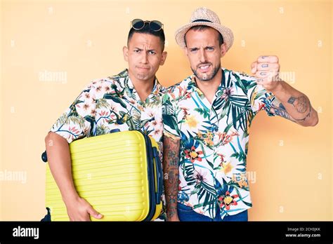 Jeune gay couple de deux hommes tenant une valise en vacances d été agacé et frustré criant avec