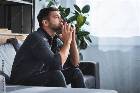 Foto De Side View Of Handsome And Pensive Man Sitting On Sofa And