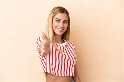 Fille blonde uruguayenne isolée sur fond beige se serrant la main pour conclure une bonne