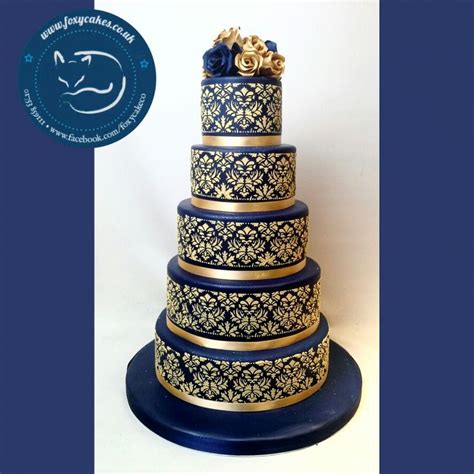 A Three Tiered Blue And Gold Wedding Cake With Flowers On It S Side