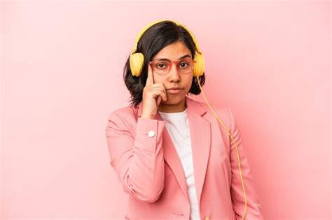 Joven latina escuchando música aislada sobre fondo rosa señalando la