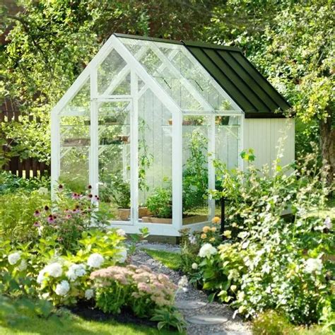 A Small White Greenhouse Surrounded By Flowers And Trees