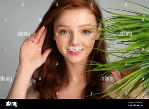 Ginger Haired Young Woman Posing With Green Plant Leaves Gray