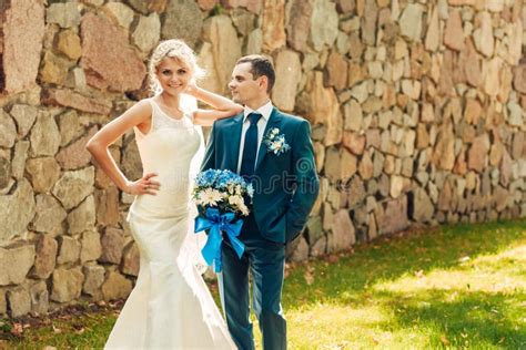 La Jeune Mariée Blonde Avec Un Bouquet Des Fleurs Dans Des Ses Mains Et Son Fiancé Se Tiennent
