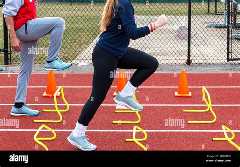 Two high school track sprinters performing sprint and form drill stepping over yellow mini ...