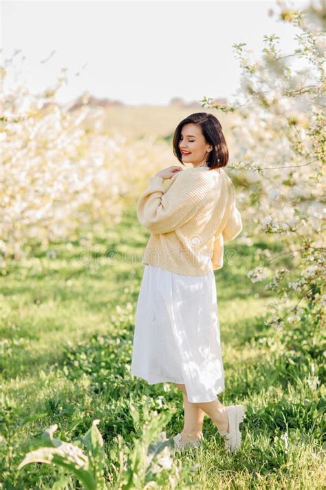 An Attractive Brunette In A White Dress In A Blooming Spring Garden Solar Glare Stock Photo