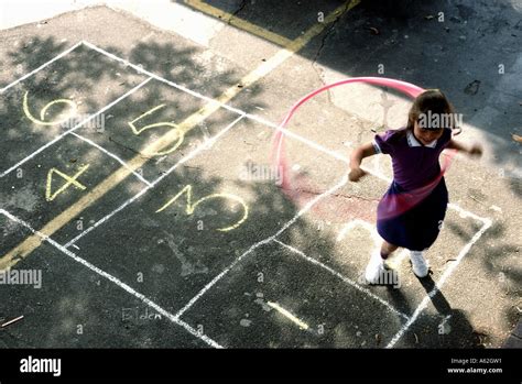 While playing hopscotch, a young girl twirls her hula hoop in a ...