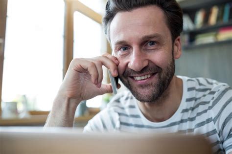 Homem de sorriso que fala no telefone móvel no café Foto Grátis