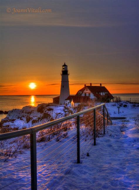 the sun is setting behind a light house in the snow by the water and fence