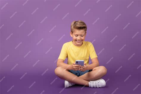 Улыбающийся мальчик-подросток смотрит на мобильный телефон, играя в ...