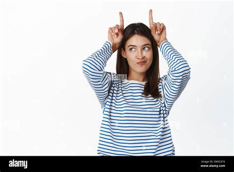 Cute And Silly Brunette Girl Points Up Shows Bull Finger Horns Gesture On Head And Looking Away