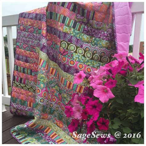 A Quilted Blanket Sitting On Top Of A Wooden Deck Next To Pink And