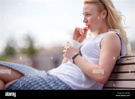 Blonde Girl Sipping Smoothie From Straw On Bench Stock Photo Alamy