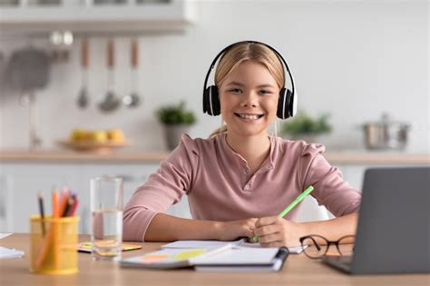 Premium Photo Cheerful European Teen Girl Blonde In Headphones Study At Home At Table With
