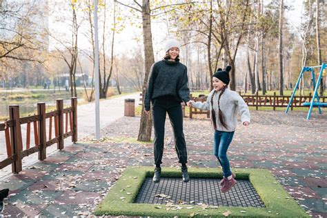 Mom And Her Daughter Jumping Together On Trampoline In Autumn Park