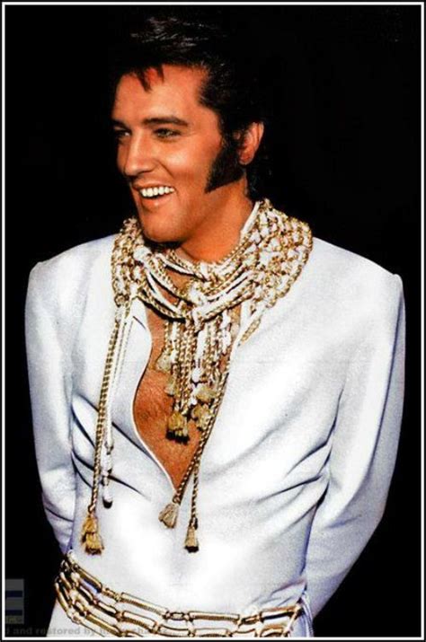 Elvis Presley In White Suit With Gold Chains Around His Neck And Chest Smiling At The Camera