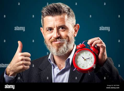 Bearded Businessman In Suit Holding Red Alarm Clock And Showing Thumb