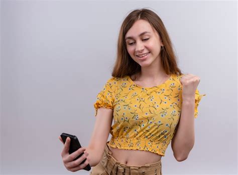 Улыбающаяся молодая девушка держит мобильный телефон с поднятым кулаком ...