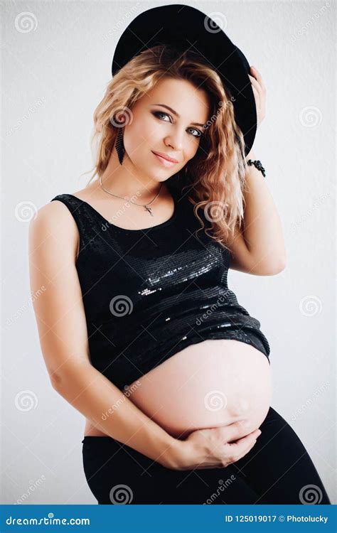 Stylish Pregnant Woman In Black Hat And Sparkling Top Embracing Her