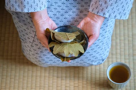 Hands Holding Japanese Kashiwa Mochi And Green Tea On Tatami Stock