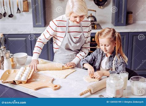 Friendly Grandmother Looking At Her Granddaughter While Making Cookies