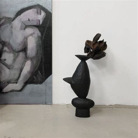 A Black Vase Sitting In Front Of A Painting On The Wall Next To A Sculpture