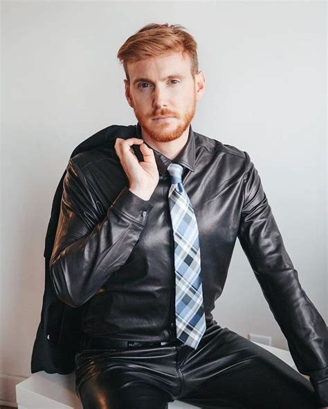 A Man With A Beard Wearing A Black Leather Jacket And Tie Sitting On A