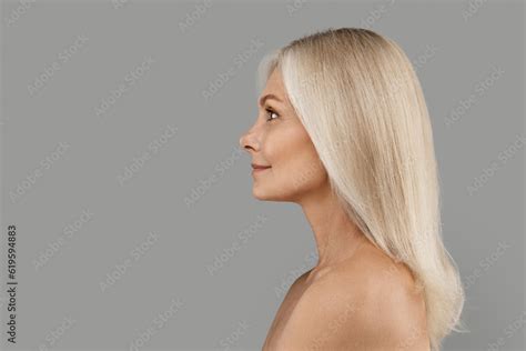 Profile Of Beautiful Mature Woman With Bare Shoulders Standing Over Grey Background Stock Photo