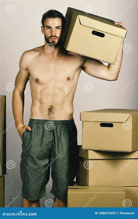 Man With Naked Torso Standing Among Cardboard Boxes And Holding One