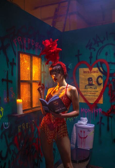 A Woman In A Red Dress Holding A Book And Standing Next To A Graffiti