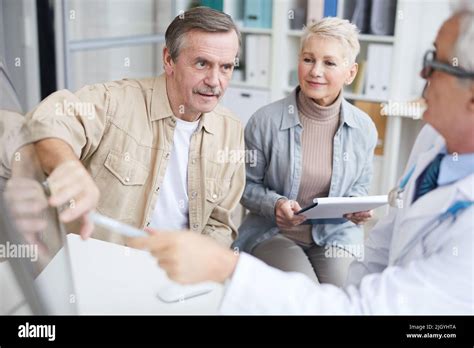 Content Mature Male Patient Pointing At Computer Monitor And Asking Doctor About CAT Scan