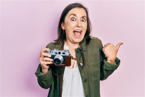 Middle Age Hispanic Woman Holding Vintage Camera Pointing Thumb Up To The Side Smiling Happy