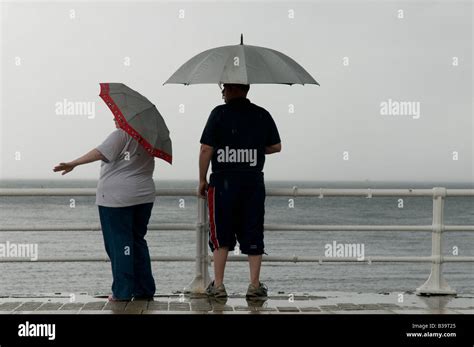 Two People Standing In The Rain Under Umbrellas On Aberystwyth Seaside