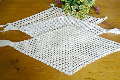 Two Pieces Of White Crocheted Cloth On A Wooden Table With Flowers In