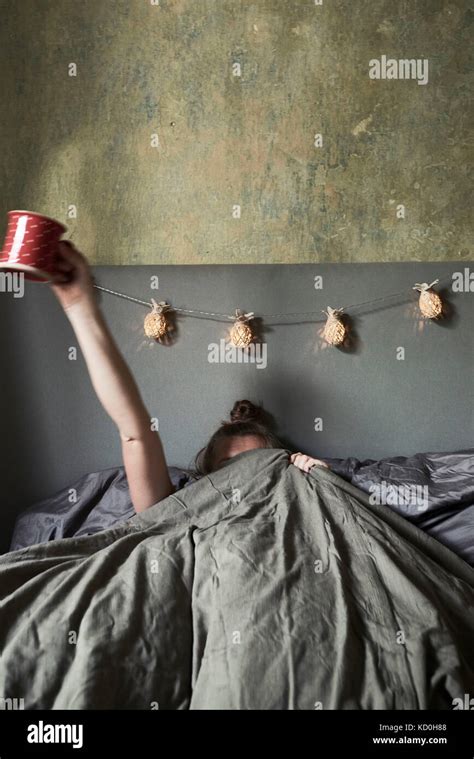 Woman in bed, hiding under covers, holding mug in air Stock Photo - Alamy