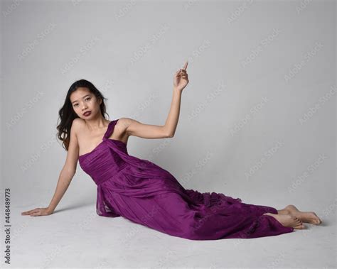 Full Length Portrait Of Pretty Brunette Asian Girl Wearing Purple Flowing Gown Sitting Pose On