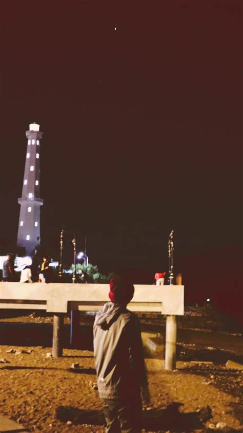 A Man Standing On Top Of A Dirt Field Next To A Tall Building At Night