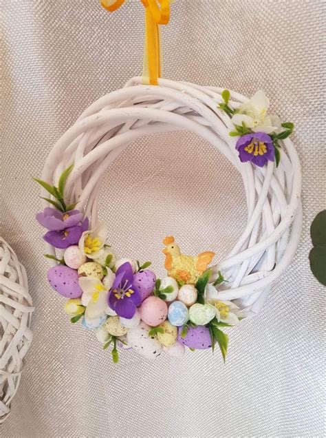 A White Wicker Wreath With Purple And Yellow Flowers On It Next To An