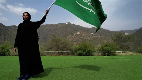 A Veiled Saudi Arabian Gulf Woman Holding The Flag Of The Kingdom Of