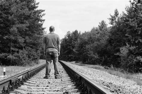 Hombre solitario caminando sobre una vía férrea tono blanco y negro