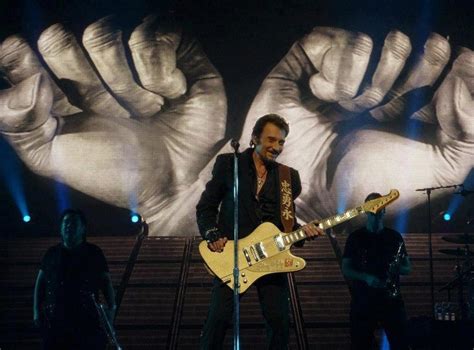 A Man Standing On Top Of A Stage With A Guitar In Front Of Two Giant Hands