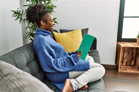 African American Woman Reading Book Sitting On Sofa At Home Stock Image