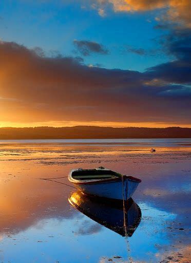 A Small Boat Sitting On Top Of A Beach Under A Cloudy Blue Sky At Sunset